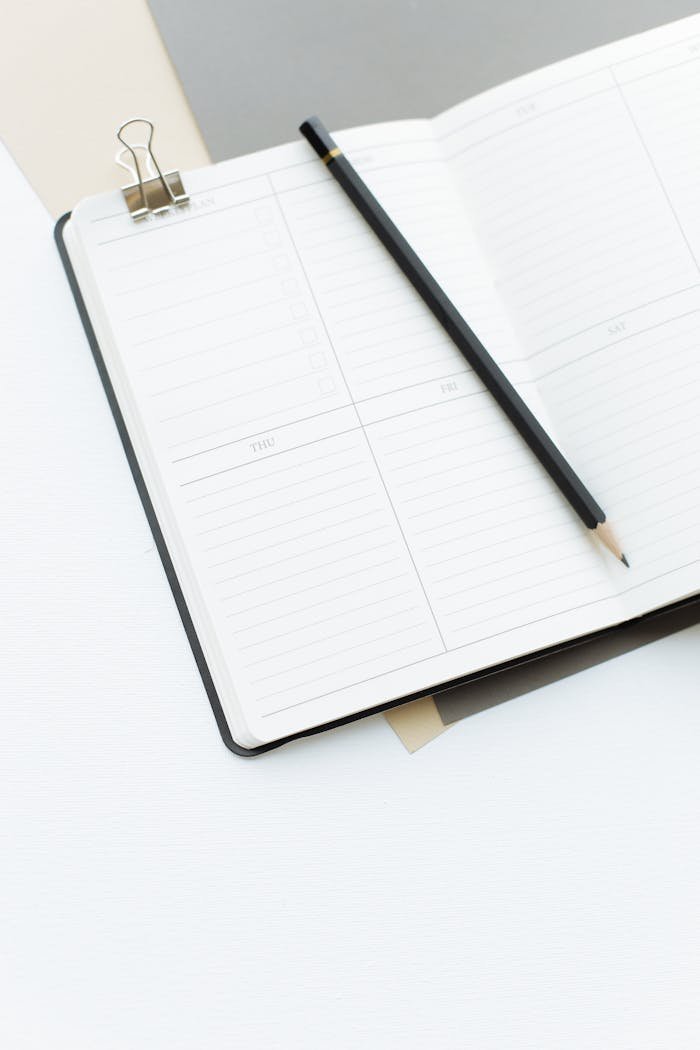 From above opened notebook with empty sheets and black pencil placed on white desk